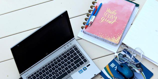 Opened laptop on a white table next to a pink notebook and white headphones